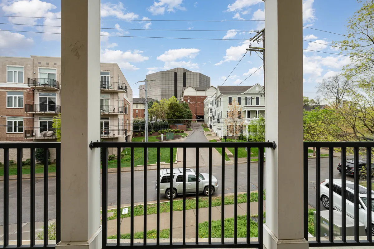 A view from the balcony looking out over the neighborhood, with the balcony railing in the foreground and surrounding buildings and streets beyond. This setting illustrates the tangible connection to the city, showing what guests might see while relaxing outside. The tranquil mood and perspective reinforce the sense of retreat above the urban landscape.