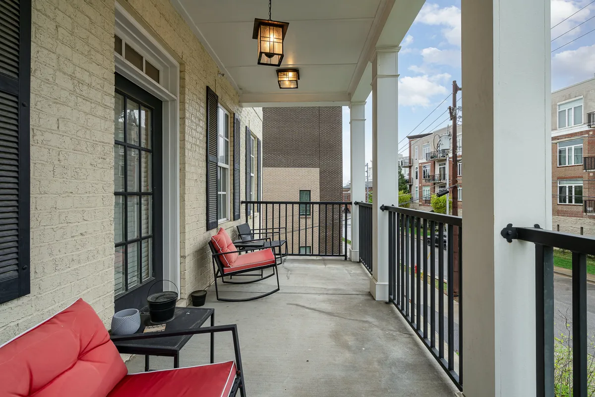 A close-up of a comfortable balcony seating arrangement with bright red chairs and a black railing, set against a classic brick wall. The ambiance feels both peaceful and connected to the outdoors, with ample space for relaxing or socializing. The image suggests a tranquil spot to enjoy the sounds and sights of the city while remaining in a private setting.