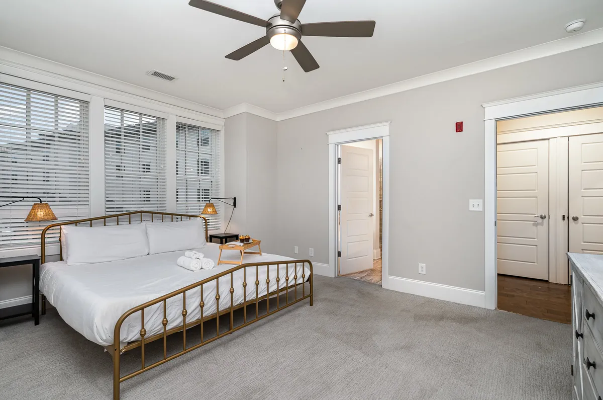 A tranquil bedroom featuring a plush bed adorned with soft bedding, a nightstand with a lamp, and doors that likely lead to a closet or en-suite bath. Natural light filters in, creating a peaceful, inviting atmosphere for rest and relaxation.