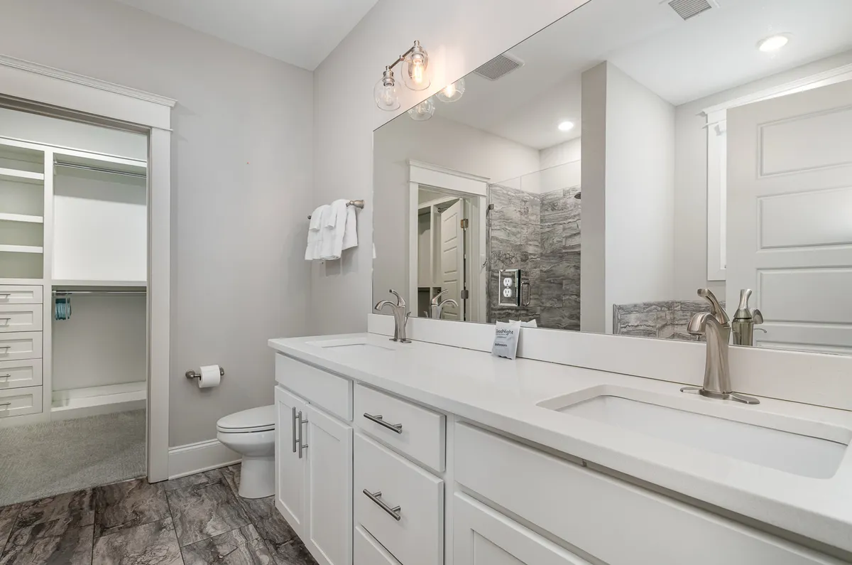 A spa-like bathroom featuring a double sink vanity with a large mirror, a visible shower area, and an entrance to a walk-in closet. The space feels tranquil and designed for both convenience and luxury.