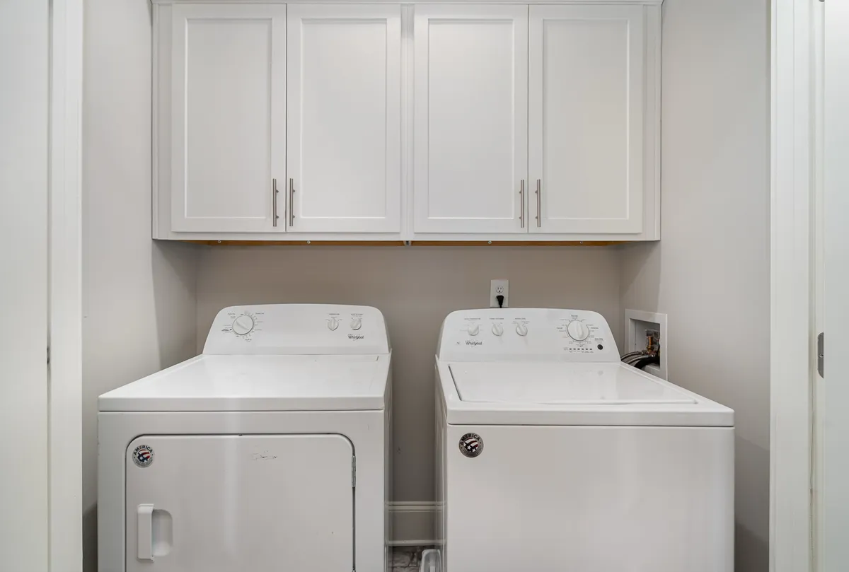 A functional laundry area displays a modern washer and dryer with upper cabinetry, highlighting practical amenities that contribute to a hassle-free stay and support the professional management aspect.