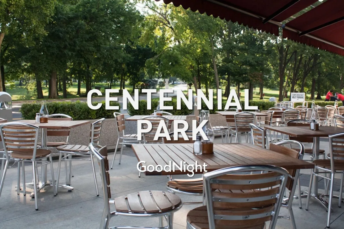 A sun-dappled outdoor seating area with wooden tables surrounded by lush greenery, where people gather to dine al fresco and enjoy the relaxed atmosphere. Sunlight filters through the trees, creating a serene, welcoming setting that feels close to nature and perfect for pet-friendly outings.
